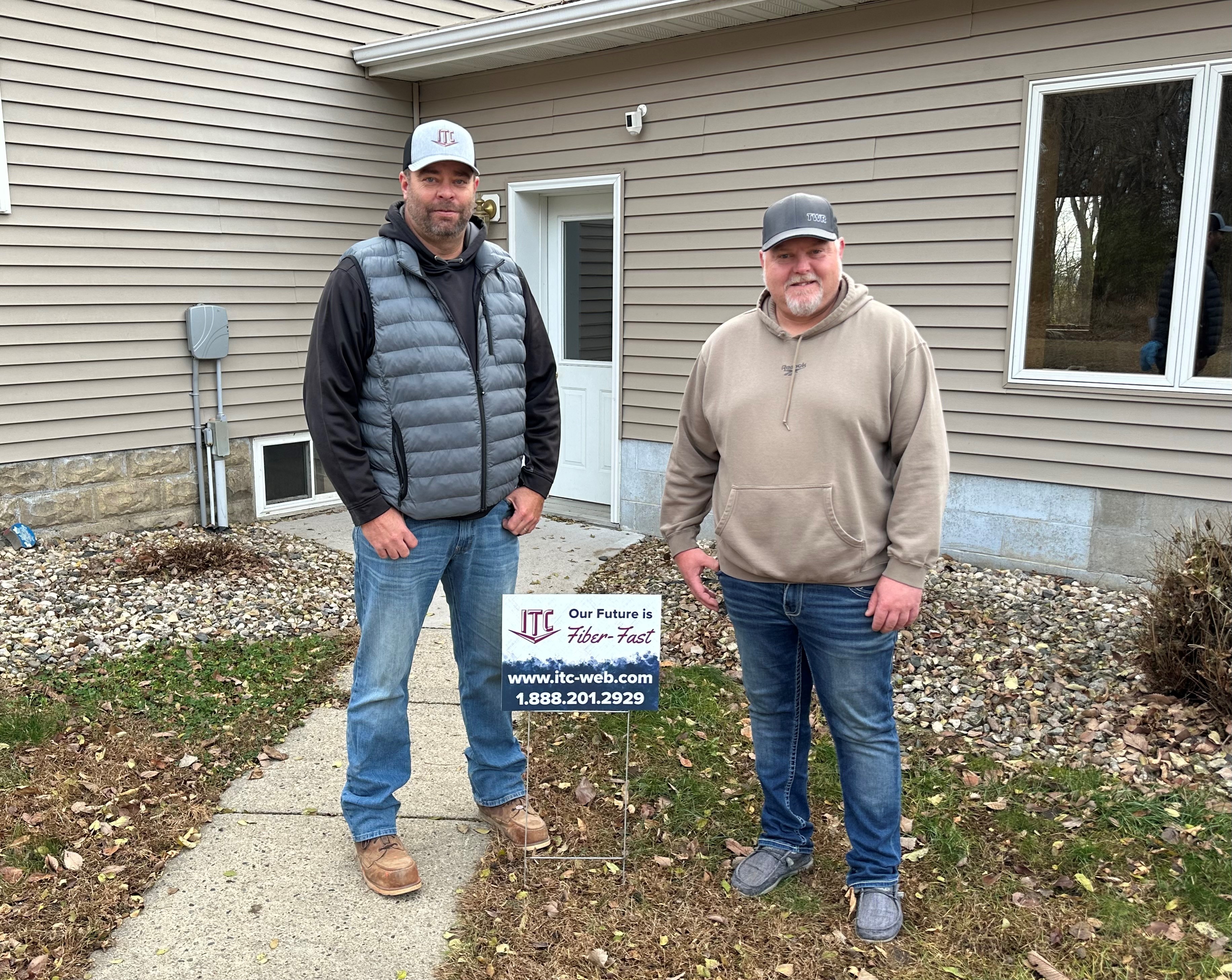 An ITC technician and the first customer of the expansion project stand in front of his home next to a yard sign that says 